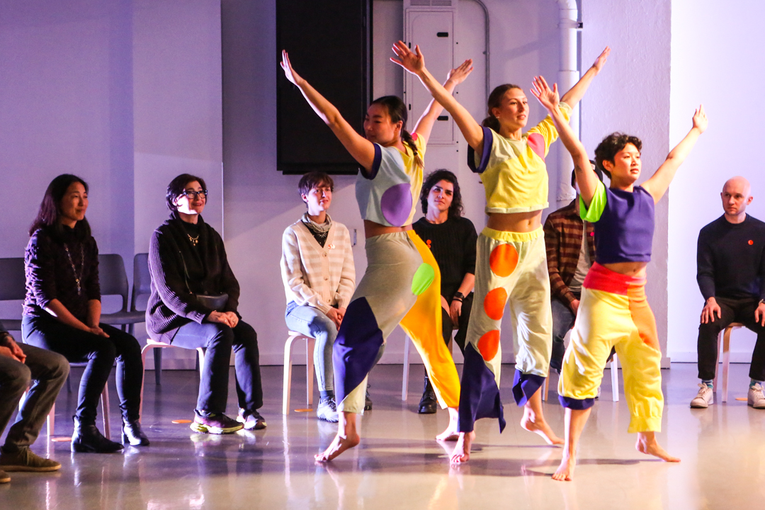 Three dancers lift their arms diagonally and hold hands in the center of the audience.